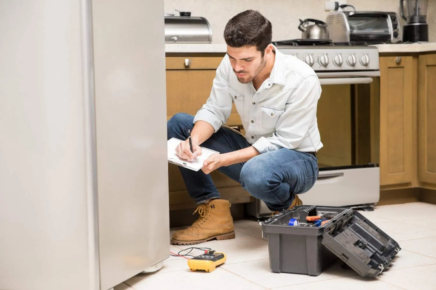 Technician writing up a repair beside a refrigerator and kitchen range