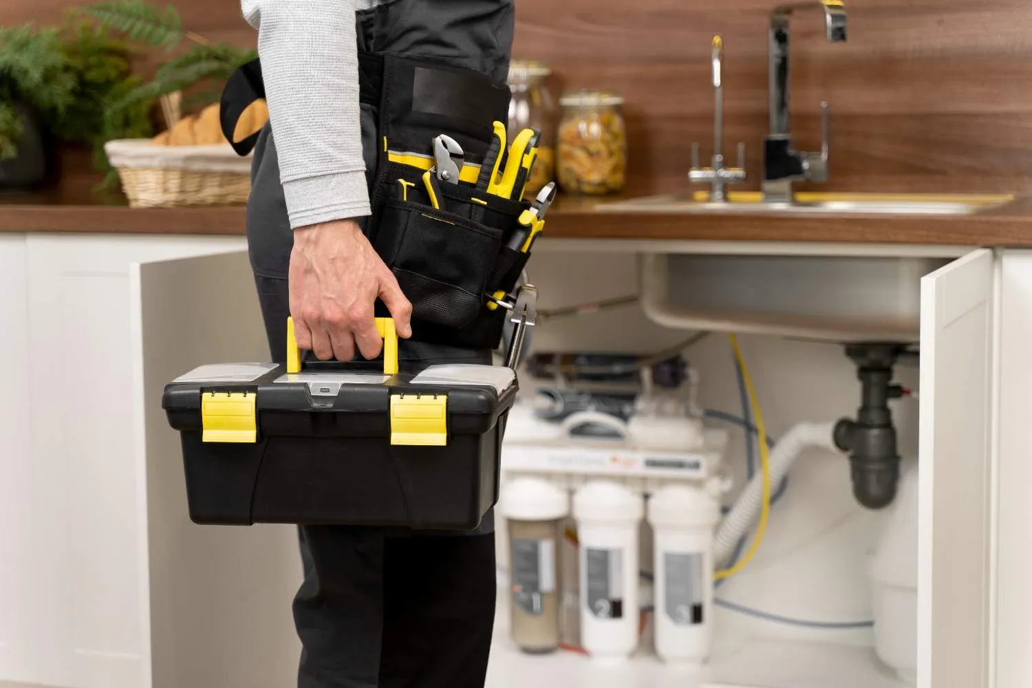 Technician carrying a toolbox beside an open cabinet under a kitchen sink